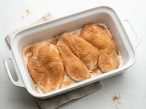 A delicious dish of salsa chicken topped with melted cheese and cilantro in a white casserole, served with tortilla chips and lime.