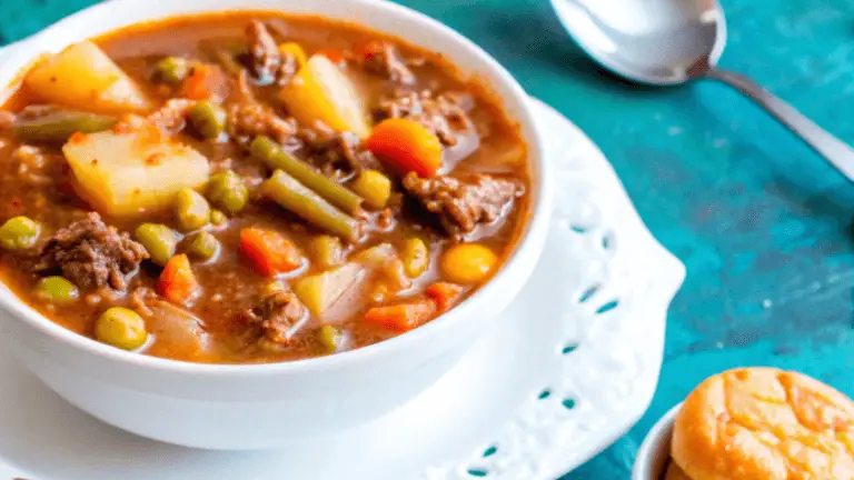 A steaming bowl of old-fashioned vegetable beef soup garnished with parsley, served with crusty bread on a wooden table.