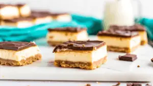  Overhead view of classic cheesecake bars with a golden crust and fresh strawberry topping on a white plate.