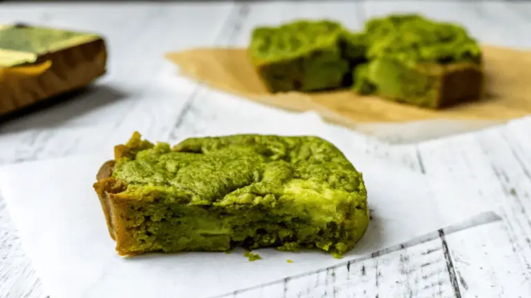 "A close-up of freshly baked matcha brownies with a vibrant green hue, topped with powdered sugar, served on a white ceramic plate."