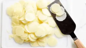 : Golden Potatoes Au Gratin in a rustic dish with a cheesy crust, garnished with thyme, placed on a wooden table