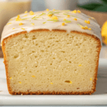 Freshly baked lemon zucchini bread with a citrus glaze and garnishes of lemon slices and zucchini, placed on a wooden board.
