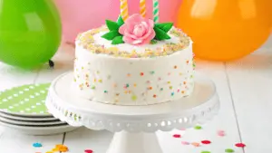 A fully decorated cake on a white pedestal with edible glitter and luster dust, styled for a celebration.