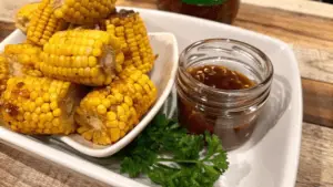 Close-up of crispy fried corn on the cob on a wooden platter with dipping sauces, garnished with parsley and lemon wedges.