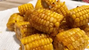 Close-up of crispy fried corn on the cob on a wooden platter with dipping sauces, garnished with parsley and lemon wedges.
