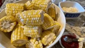 Close-up of crispy fried corn on the cob on a wooden platter with dipping sauces, garnished with parsley and lemon wedges.