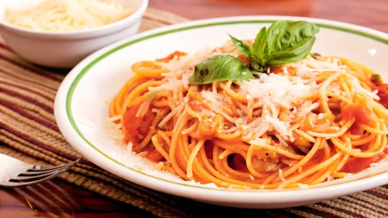 "A plate of spaghetti in tomato basil sauce garnished with fresh basil leaves and Parmesan cheese, served on a rustic wooden table with tomatoes, garlic, and olive oil in the background."