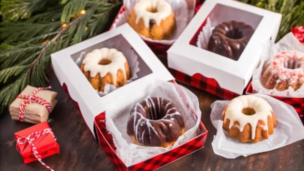 "Mini bundt cakes with a golden-brown exterior, topped with pink glaze and placed on pink plates, with one displayed on a white cake stand against a soft pink marble background."