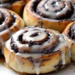 Close-up of freshly baked Oreo Stuffed Cinnamon Rolls with a golden-brown exterior, swirled with crushed Oreo cookies, and drizzled with a smooth, creamy glaze. The rolls have a soft, fluffy texture with a rich cookies-and-cream filling.