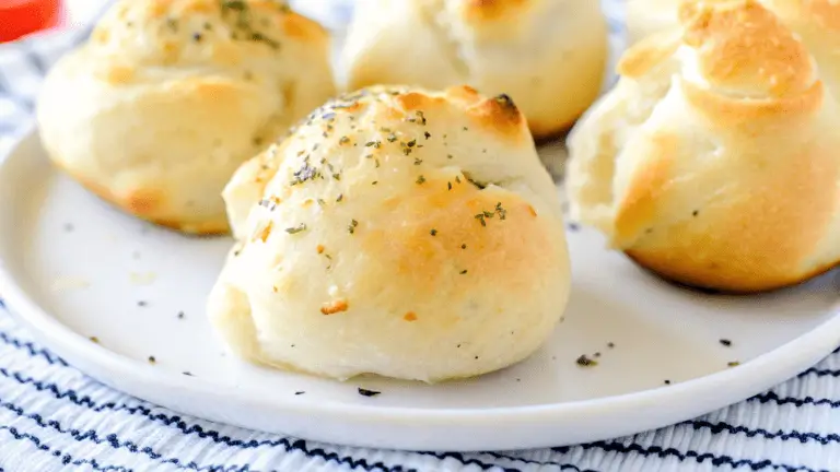 Golden-brown air fryer pizza bombs on a white plate, garnished with herbs and melted cheese, placed on a striped kitchen towel.