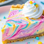 A slice of Easter Swirl Pie on a beige plate, featuring a creamy white filling with a graham cracker crust, topped with pastel-colored whipped cream swirls and festive sprinkles. In the background, the full pie and additional slices are visible, along with a soft blue napkin and scattered sprinkles for a festive touch.