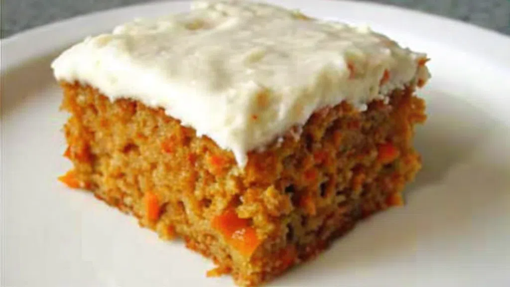 Alt Text: A sliced sugar-free carrot cake topped with white frosting and garnished with walnuts, served on a white plate.