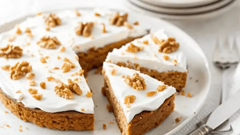 Alt Text: A sliced sugar-free carrot cake topped with white frosting and garnished with walnuts, served on a white plate.