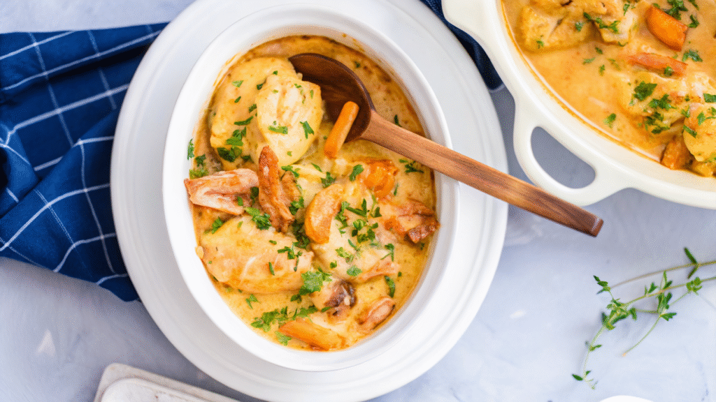 “Creamy slow cooker chicken stew with carrots, potatoes, and herbs served in a white crockpot and plated in a white bowl, garnished with chopped parsley.”