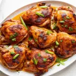 Honey Lemon Ginger Glazed Chicken in cast iron skillet with lemon slices and fresh herbs, golden-brown and glazed to perfection