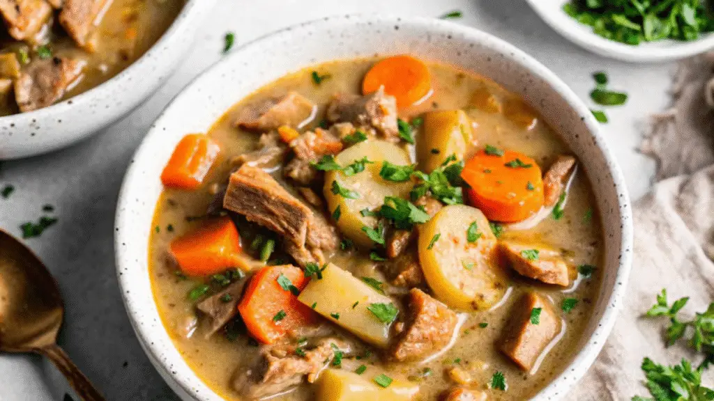 “Bowl of slow cooker chicken stew with tender chicken pieces, carrots, potatoes, and fresh parsley, served in a rustic white bowl”